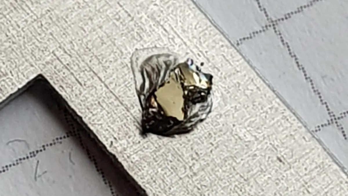 Pequeño cristal laminar de brillo metálico, de la familia de los dicalcogenuros, sobre una placa de metal