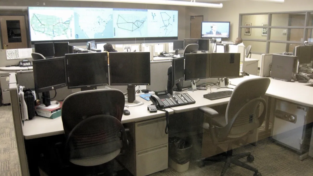 Centro de operaciones de red con escritorios, monitores y una pantalla mural con mapas de conexiones