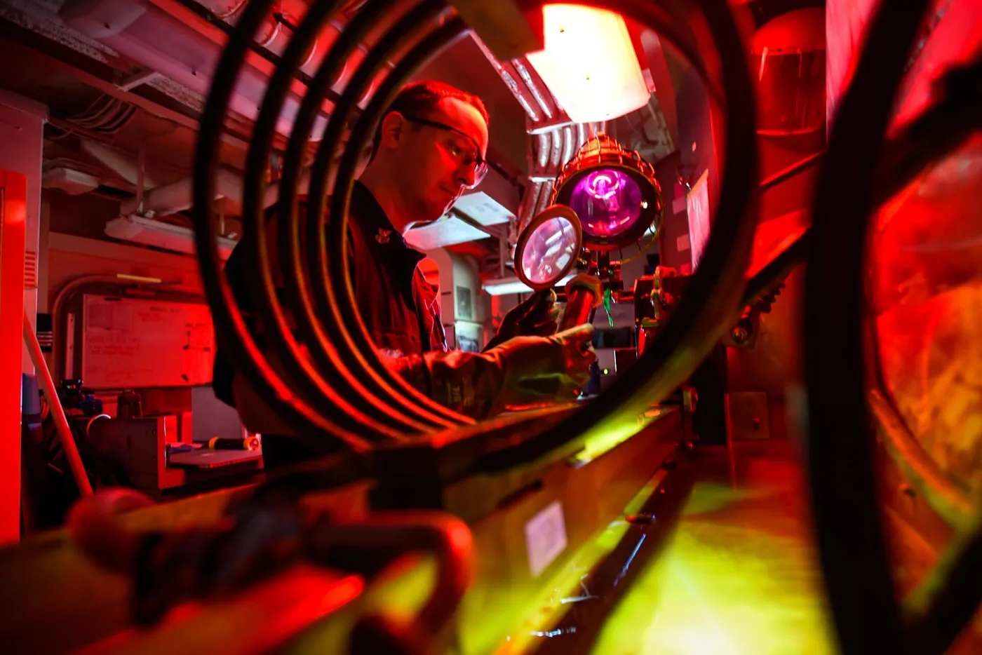 A sailor looks through a magnifying glass in a blue US Navy uniform