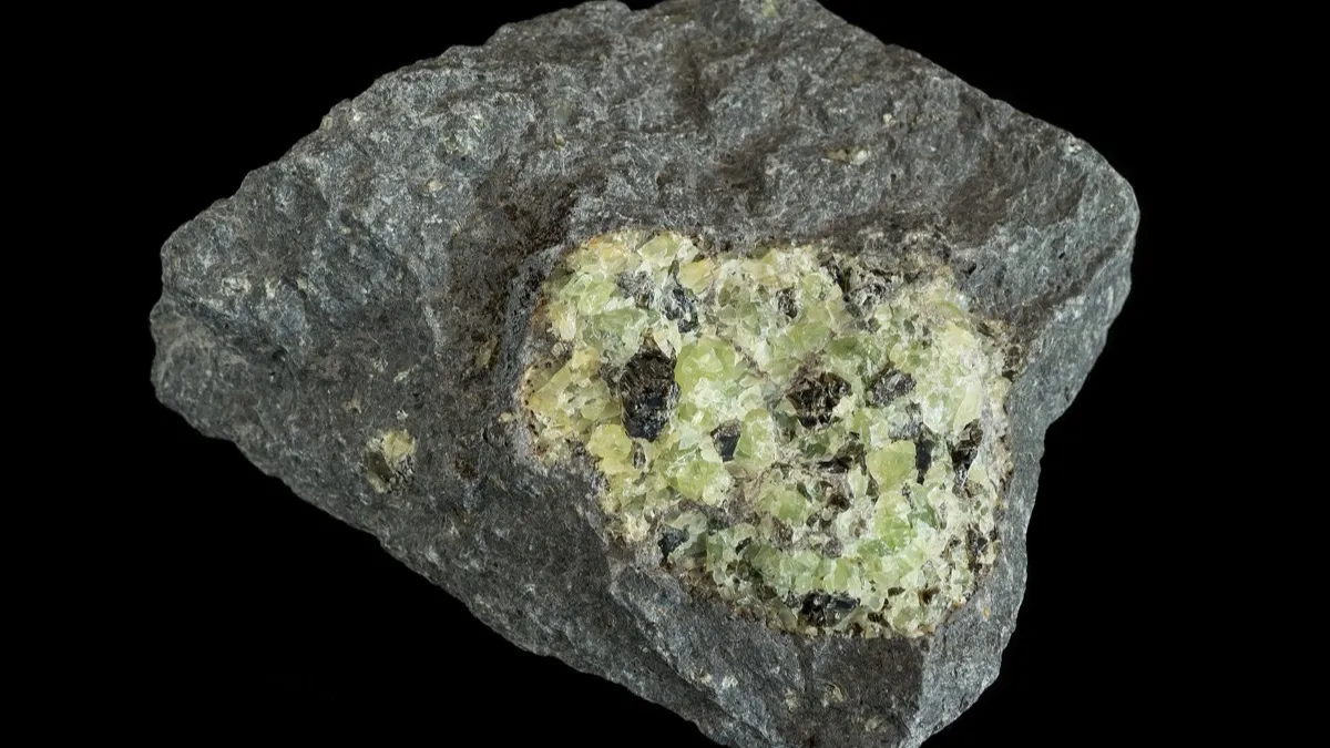 Nódulo de olivino de color verde amarillento incrustado en una roca de basalto oscura