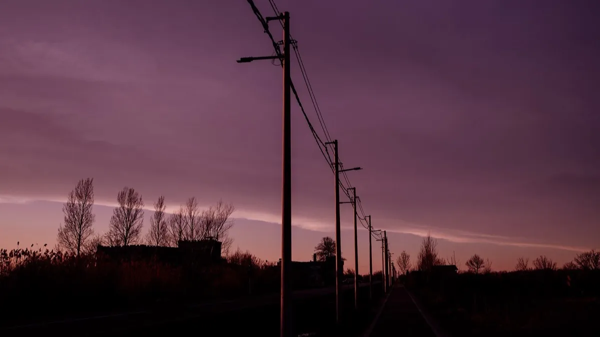 Siluetas de postes y cables eléctricos contra un atardecer de tonos morados